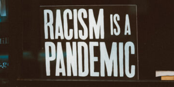 A sign in a window that reads Racism is a Pandemic. Photo by Jon Tyson