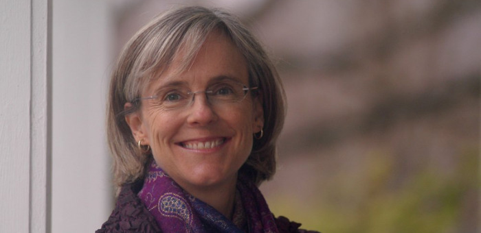 Photo of WDN member Sage Wheeler, a white women wearing glasses and a purple scarf. She has shoulder-length grey hair and smiles at the camera.