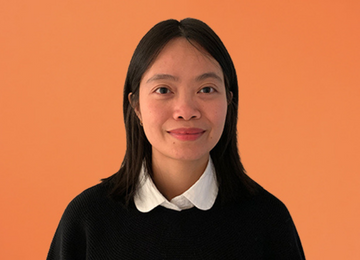A photo of Jenna Le. She is a Vietnamese woman with shoulder length black hair. She wears a white collared shirt, black sweater, and smiles at the camera