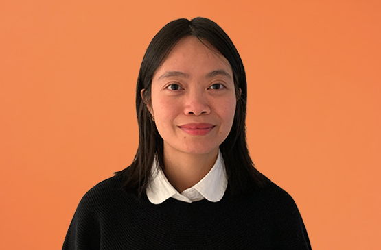 A photo of Jenna Le. She is a Vietnamese woman with shoulder length black hair. She wears a white collared shirt, black sweater, and smiles at the camera