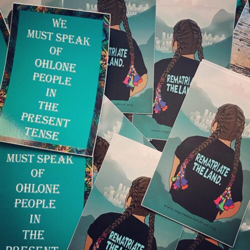 A photo of flyers with the words "we must speak of Ohlone people in the present tense" and of a graphic of a person with long braided hair wearing a t-shirt that reads "rematriate the land"