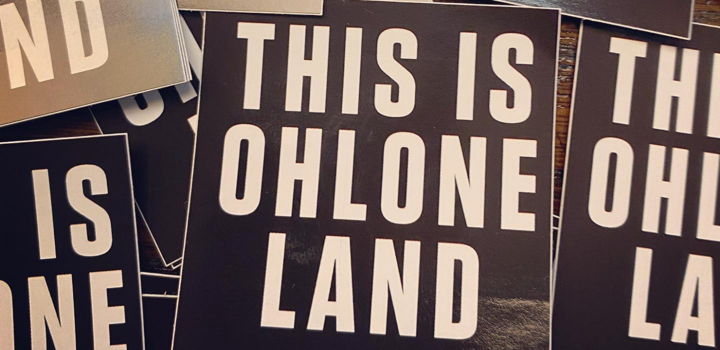 a picture of a pile of stickers that say "this is Ohlone land" in large white block letters