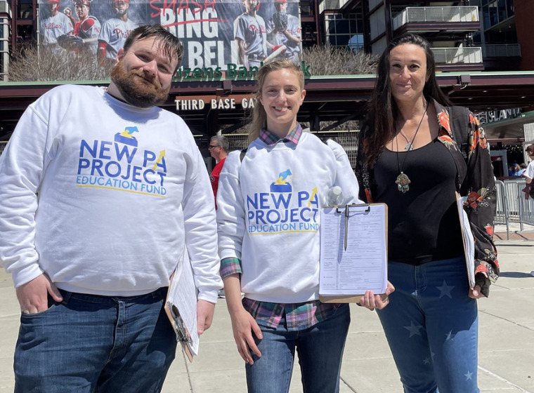 Photo of three people with clipboards standing in a crowded area wearing New PA Project shirts